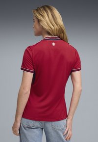 Polo rouge à manches courtes avec un col contrastant et des accents aux manches, ornée d'un petit emblème au dos, fabriquée en tissu respirant.