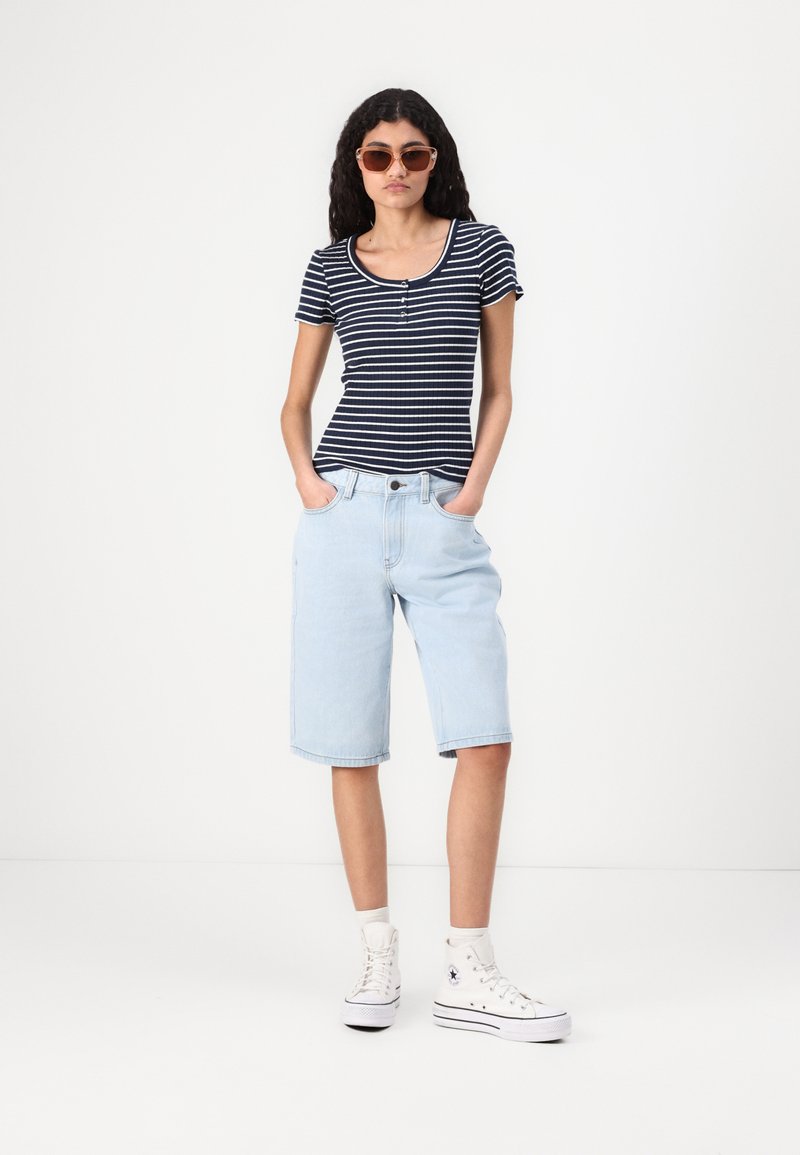 T-shirt fitted à rayures bleues et blanches associé à un short en denim bleu clair à coupe droite. Des baskets montantes blanches complètent le look.