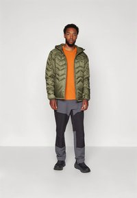 Maslinasto zelena puhasta jakna sa patentnim zatvaračem, narančasta majica s okruglim izrezom, sive i crne teksturirane hlače te crne cipele. Opuštena dnevna odjeća za van.