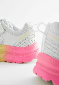 Białe buty sportowe z teksturowaną cholewką, z różowym gradientowym bieżnikiem oraz tęczowymi akcentami w kształcie zygzaka. Zawierają rzep.
