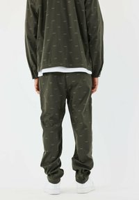 Camisa de manga larga color verde olivo y pantalones a juego con pequeños patrones del logo "PXP". Corte relajado con puños elásticos y cinturilla. Camiseta blanca de capa debajo.