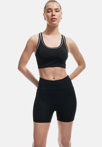 Reggiseno sportivo nero con rifiniture bianche e pantaloni corti high-waisted abbinati. Il tessuto appare liscio ed elasticizzato, progettato per l'abbigliamento sportivo.
