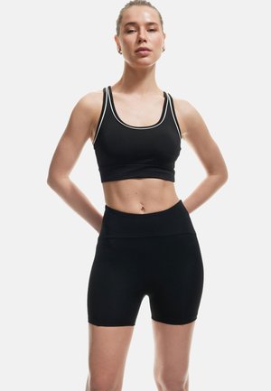 Schwarzer Sport-BH mit weißen Akzenten und passenden hochtaillierten Shorts. Der Stoff wirkt glatt und dehnbar, entworfen für sportliche Aktivitäten.