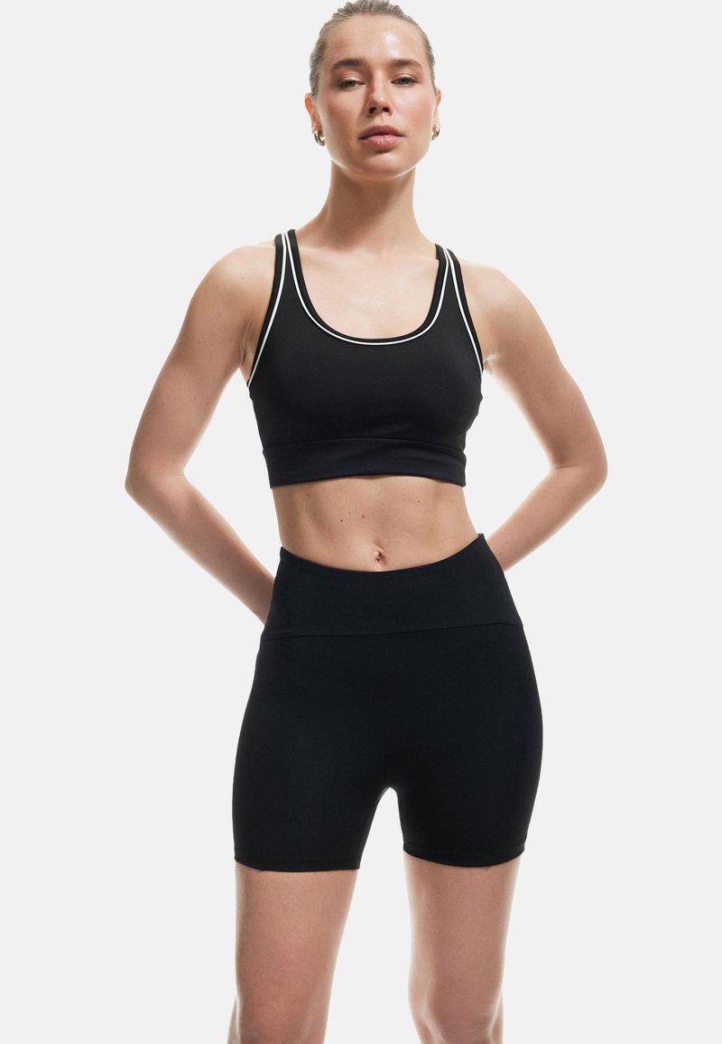 Reggiseno sportivo nero con rifiniture bianche e pantaloni corti high-waisted abbinati. Il tessuto appare liscio ed elasticizzato, progettato per l'abbigliamento sportivo.