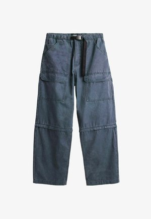 Tummanharmaat kuorihousut, joissa useita taskuja, säädettävä vyötärönauha mustalla solkivyöllä ja irrotettavat lahkeet monikäyttöisyyttä varten.