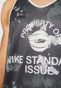 Black mesh sleeveless tank top featuring a white graphic text "PROPERTY OF NIKE STANDARD ISSUE" with a circular logo and distressed accents.