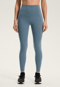 Visoko pasne, oprijete pajkice iz mehke modre tkanine. Imajo šive vzdolž nog in so kombinirane s črnimi športnimi copati.