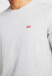 Šedé bavlněné tričko s kulatým výstřihem a krátkými rukávy. Na hrudi je malá nášivka červeného loga Levi's. Měkká struktura.