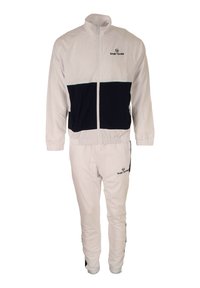 Witte trainingsoutfit met een marineblauwe horizontale streep, bestaande uit een ritsjack en bijpassende broek. Logo op het jack en de broek in het zwart.