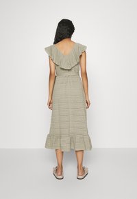 Bezramínková světle zelená šaty s volánkovým výstřihem a stupňovitou spodní částí. Vyrobené z texturované látky s jemným vzorem. Ploché boty s mašlemi.