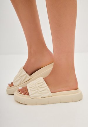 Infradito trapuntate beige con suola spessa e finitura texturizzata, design aperto sul retro e dettagli di cucitura discreti sulle cinghie.