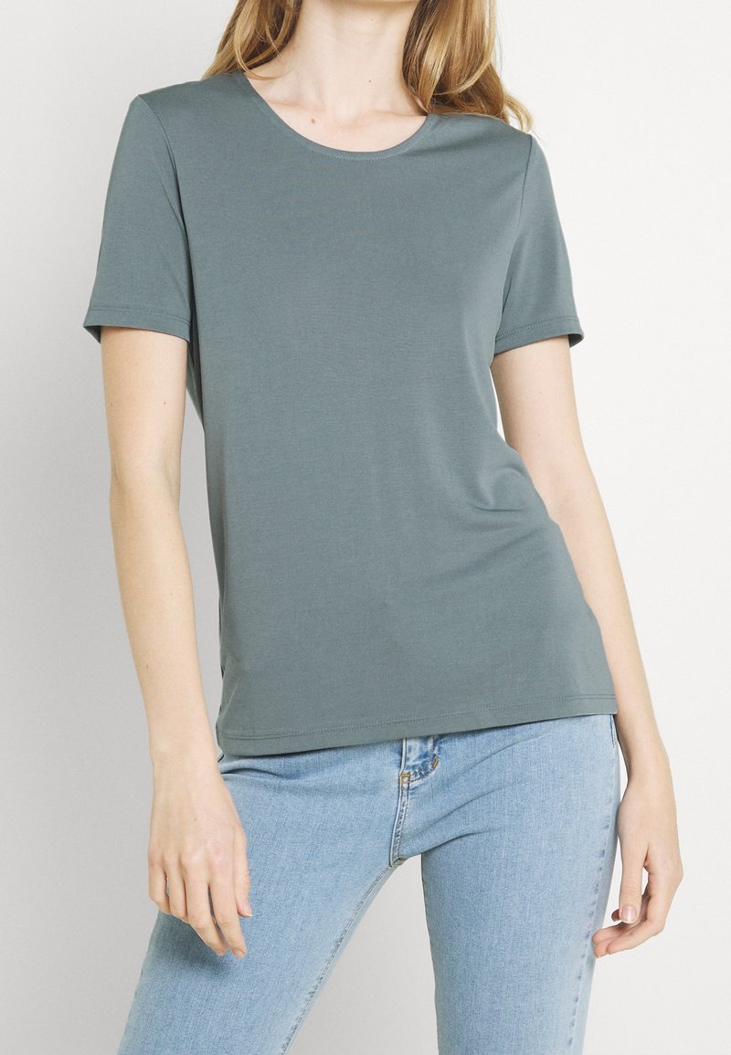 T-shirt gris à manches courtes avec un col rond, texture lisse et coupe ajustée. Porté avec un jean bleu clair.