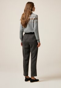 Suéter de punto gris con un yugo estampado, combinado con pantalones de cuadros gris oscuro. El modelo lleva zapatillas negras sin cordones, posando sobre un fondo neutro.