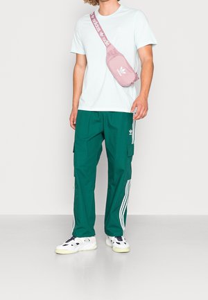 Lichtblauwe t-shirt met korte mouwen, groene cargo broek met witte strepen, roze schoudertas en witte sneakers met zwarte accenten.