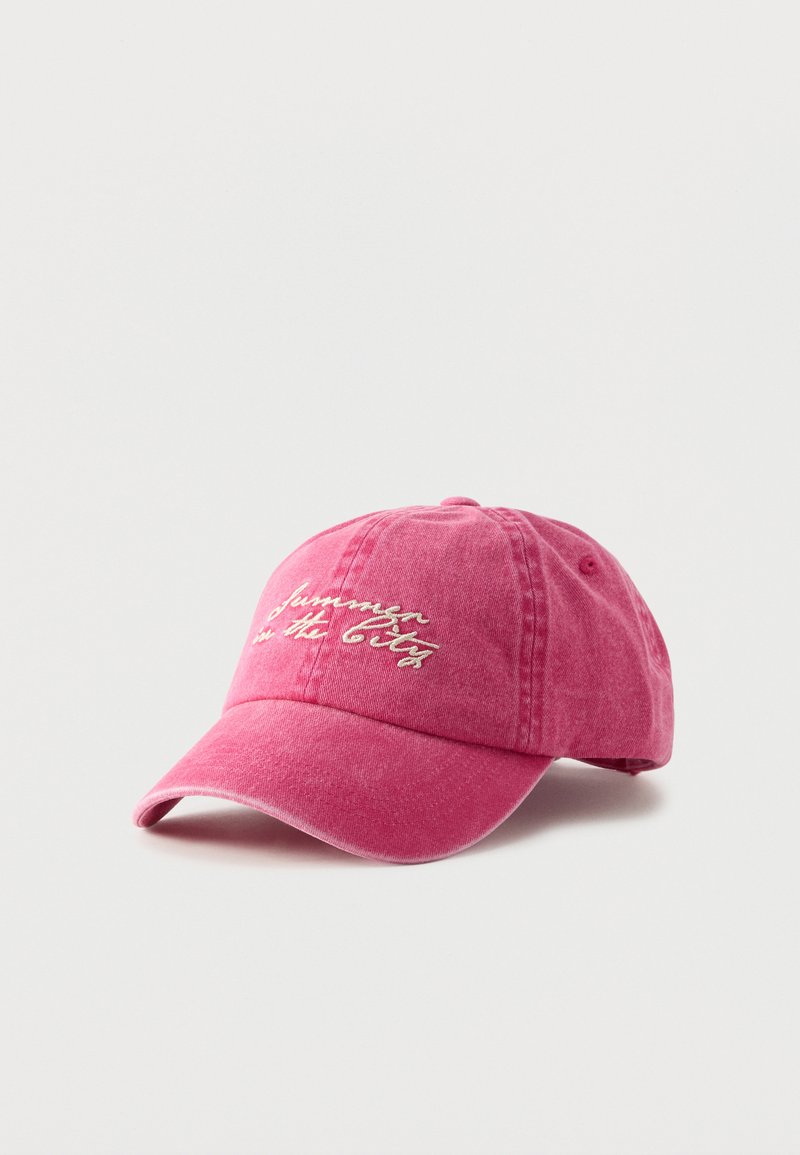 Casquette de baseball rose avec texte cursif brodé blanc « summer in the city » sur le devant, affichée sur un fond clair uni.