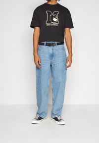 Černé bavlněné tričko s grafikou medvěda, světle modré volné džíny, černý opasek a černé tenisky s bílou podrážkou. Jednoduchý casual outfit.