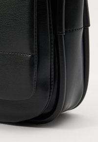 Black leather bag with a smooth texture and rounded edges; features a stitched panel and a front pocket for added detail.