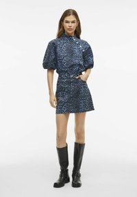 Blauwe panterprint jurk met korte pofmouwen, knoopdetails en een getailleerde taille. Gecombineerd met zwarte leren laarzen tot de knie.