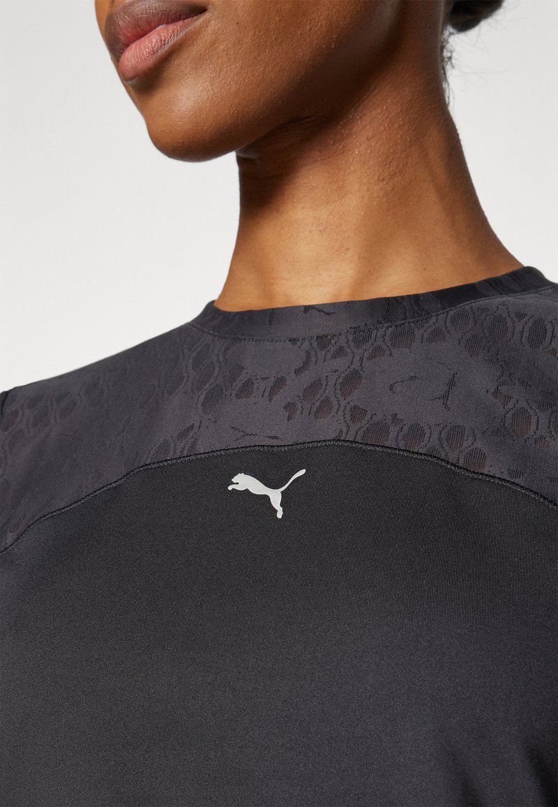 Zwarte sportshirt met een gestructureerd donker patroon op de schouders en een wit Puma-logo op de borst. Glad stof en een aansluitend ontwerp.