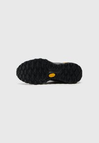 Svart utendørs såle laget av gummi med et teksturert grep mønster og fremtredende gult "Vibram"-logo. Har trekantede og heksagonale dekk.
