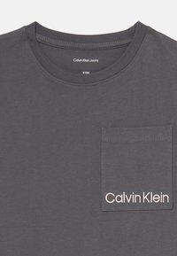 Szara bawełniana koszulka z okrągłym dekoltem, krótkimi rękawami i kieszonką na lewej piersi, z białym haftem 'Calvin Klein'.