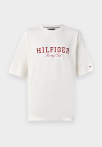 Λευκό μπλουζάκι κοντό μανίκι από διχτυωτό ύφασμα με κόκκινο κείμενο "HILFIGER Racing Club" και μια μικρή σημαία Tommy Hilfiger στο αριστερό μανίκι.