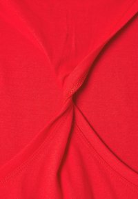 Top sin mangas de color rojo con una textura suave y lisa. Presenta un diseño retorcido en la parte frontal y costuras reforzadas a lo largo de los bordes.