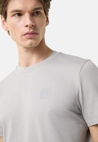 Lysegrå t-shirt med rund halsudskæring og et diskret præget logo på brystet. Glat, blødt stof med en tætsiddende pasform.