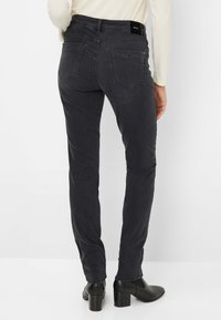 Jeans neri slim fit con una superficie liscia, dotati di tasche posteriori e vita alta media. Abbinati a stivaletti neri con tacco.