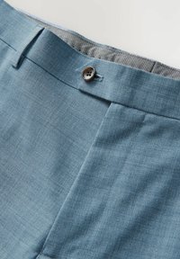 Helleblaue Hose aus strukturiertem Stoff, mit einem braunen Knopf und einem kontrastierenden gemusterten Futter. Flach vorne mit seitlichen Taschen.