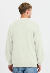 Suéter verde claro, textura de punto, corte relajado, hombros caídos, puños y dobladillo acanalados, combinado con jeans azules, diseño sencillo.