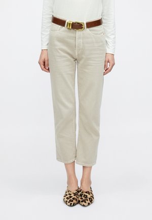 Jeans beige corti con tasche frontali, abbinati a una cintura marrone con fibbia dorata. Indossati con scarpe slip-on con stampa leopardata.