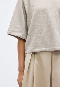 Pull beige à manches courtes en tissu tricoté doux avec un ourlet côtelé, assorti à une jupe plissée beige en matière légère.