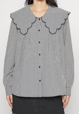 Blouse vichy noire et blanche avec grand col festonné, boutons noirs sur le devant et manches longues bouffantes avec poignets boutonnés.