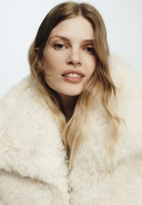 Cappotto in pelliccia sintetica bianco e soffice, con un ampio colletto, caratterizzato da una morbida texture e una vestibilità comoda. Il tessuto sembra caldo e accogliente.