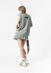 Vestido gris sin mangas con dobladillo plisado, hecho de un tejido texturizado. Presenta una etiqueta negra en la parte posterior y una etiqueta larga colgando de la falda.