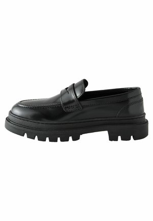 Mocassins en cuir noir avec une semelle en caoutchouc épaisse et une sangle surélevée à l'avant. Présente des coutures visibles et une finition lisse.