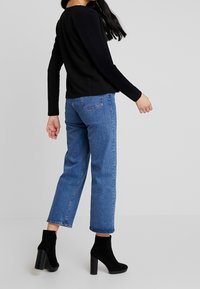 Czarny, prążkowany top z długim rękawem w zestawieniu ze jasnoniebieskimi spodniami o prostym kroju i czarnymi zamszowymi botkami za kostkę na szerokim obcasie.