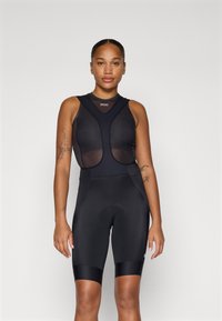 Svart sykkelantrekk med mesh-overdel med V-hals-design og polstrede shorts. Glatt tekstur med subtil merkevare og tettsittende silhuett.