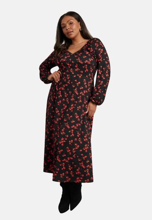 Schwarzes Blumenkleid mit roten Mustern, V-Ausschnitt, langen Ärmeln und fließender Silhouette. Kombiniert mit schwarzen Ankle Boots.