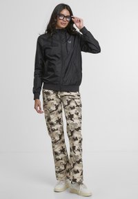 Black lightweight jacket with a zip front and hood, paired with camouflage cargo pants in beige and olive tones, featuring side pockets.