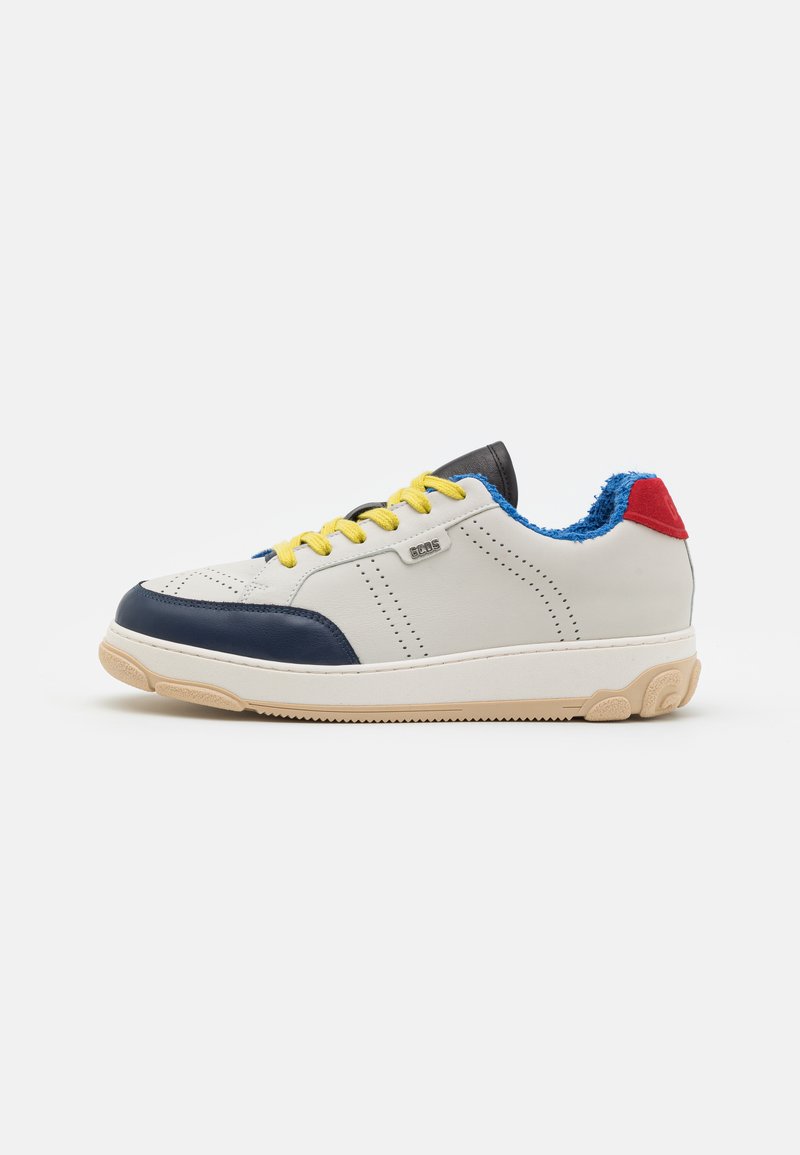 Baskets blanches avec des accents bleu marine, des lacets jaunes, un talon rouge et un col bleu. Présente des perforations et une semelle en caoutchouc texturée.