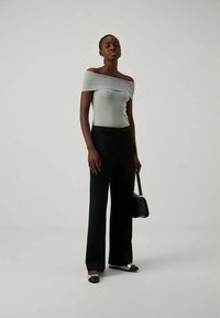 Top cano off-white claro, com nervuras, combinado com calças largas pretas e calçado preto. Modelo segurando uma pequena mala preta.