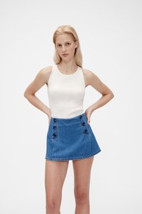 Valge ribakujuline tank top koos sinise teksaminituodega, millel on mustad nööbid ja kõrge vöökohaga disain. Sile tekstuur.