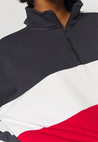 Sweat-shirt zippé avec blocs de couleurs bleu marine, blanc et rouge, doté d'un col montant et d'une texture douce.