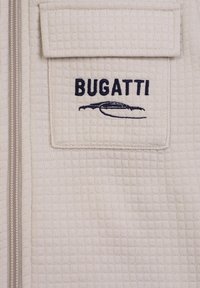 Giacca Bugatti con zip in tessuto beige chiaro testurizzato con tasca sul petto; presenta logo ricamato blu navy e dettagli.