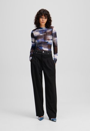 Long-sleeve mesh top with blue and black abstract pattern, paired with loose black trousers and blue pointed heels. Features a logo on the chest.
