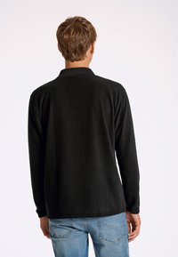 Svart ribbad långärmad tröja med krage, med en texturerad tyg och avslappnad passform, kombinerad med ljusblå jeans.