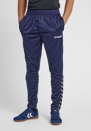 Marineblauwe sportbroek met een gestructureerde afwerking, elastische tailleband, zijzakken en zwarte chevronaccenten langs de buitenzijde van het been.
