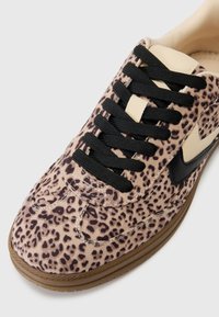 Leopard print sneaker with a suede texture, black laces, and brown rubber sole. Features a beige accent on the side and stitching details.